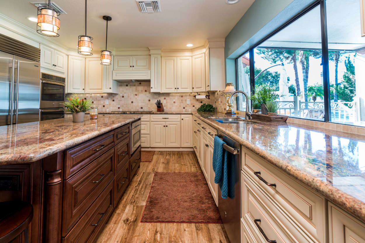 Brown and cream kitchen with wood flooring, granite countertops, and tiled backsplash.