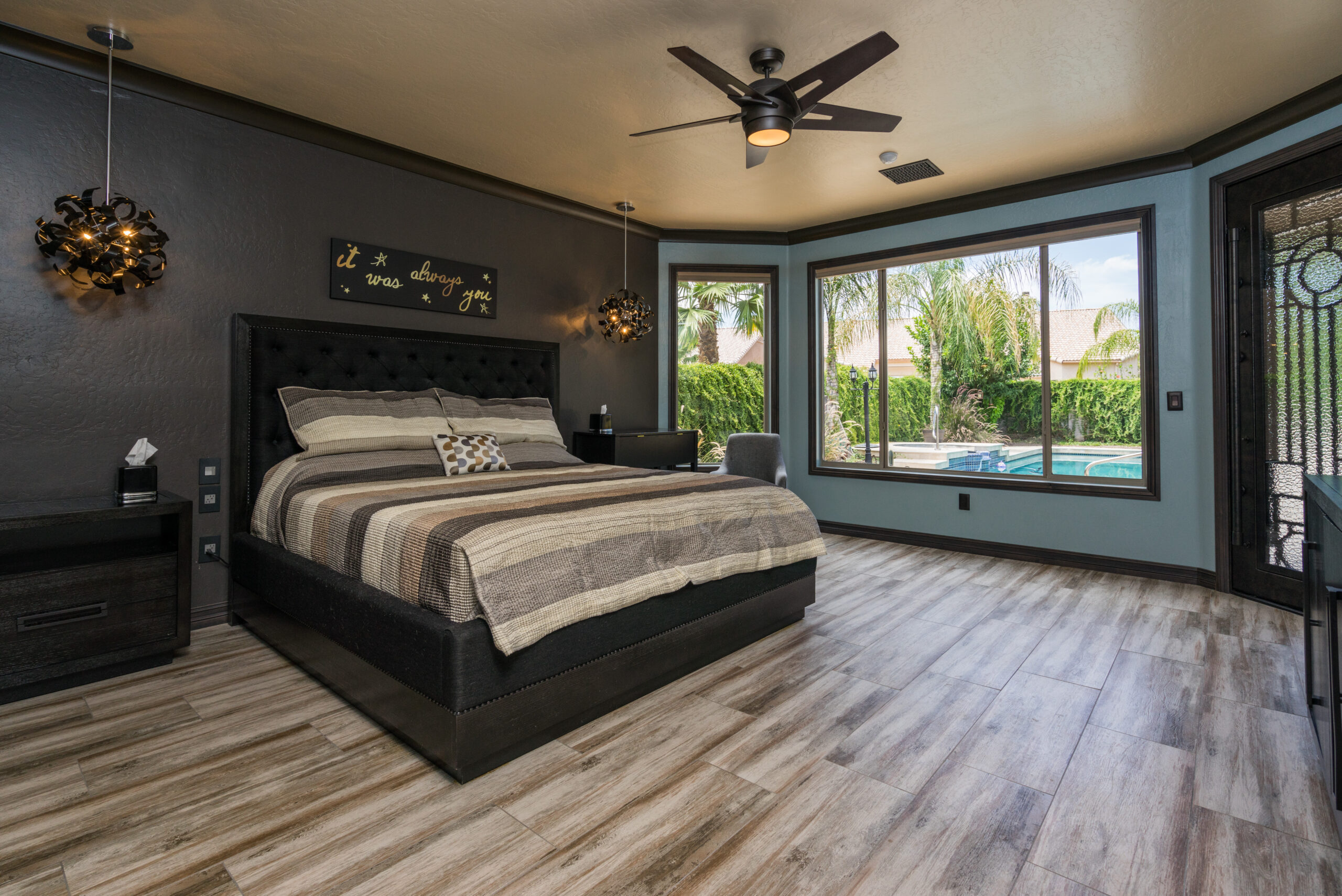 Master bedroom with dark tones and window overlooking swimming pool.